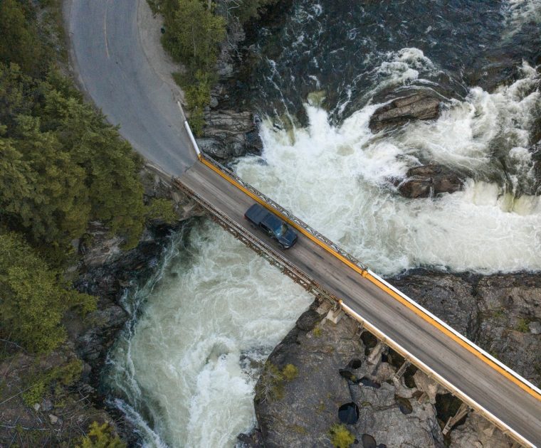 Drone photo of a truck driving over a bridge with a river below.