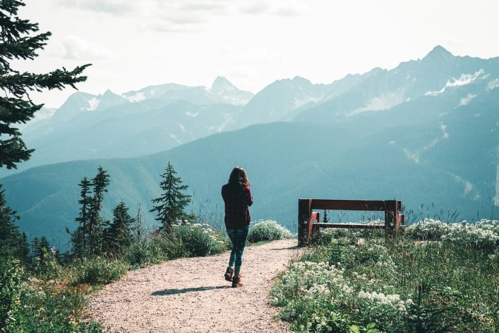 Woman walking along a hiking trails in Revelstoke Mountain Resort with wildflowers and mountains surrounding the trail